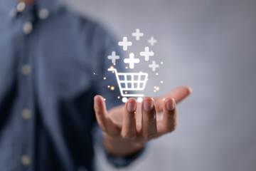 Technology online shopping business concept of a businessman hand holding virtual trolley cart icons with a plus sign symbol to add or receive an order.