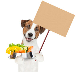 jack russell terrier puppy holds bowl of vegetables and empty placard. isolated on white background