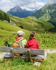 Zwei Teenager sitzen auf einer Bank und genießen den herrlichen Ausblick ins Gebirge - obrazy, fototapety, plakaty