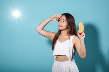 Beautiful Asian young woman holding body lotion on hand in studio shot isolated on blue background,...