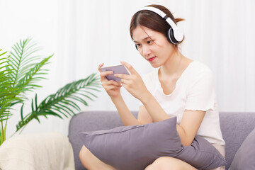 Obraz premium Lifestyle in living room concept, Young Asian woman in headphone to playing games on smartphone