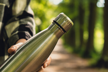 Close-up of Unrecognizable female hand holding Water bottle. Reusable steel thermo water bottle in...