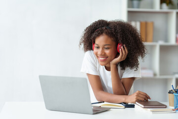 Beautiful young woman student wearing headphones is video chatting on laptop, smiling faces and gestures happily studying.