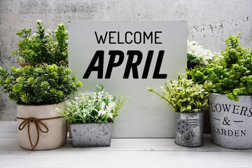 Welcome April text message with artificial plant decoration on wooden background