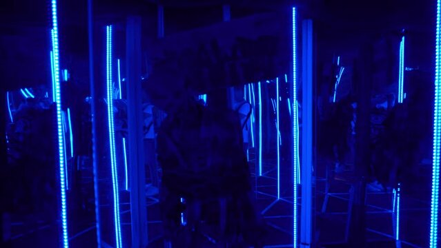 Scary skeleton scares visitors in mirror maze. Amusement park. Mirrors distort reality. Young woman in infinity metaverse. Interactive room with colorful fluorescent tube illumination.