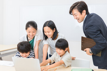 休み時間にパソコンで遊ぶ小学生の子供達と先生（学校・塾）
