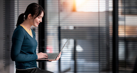 Cheerful young female designer smiling and working on computer laptop at office.