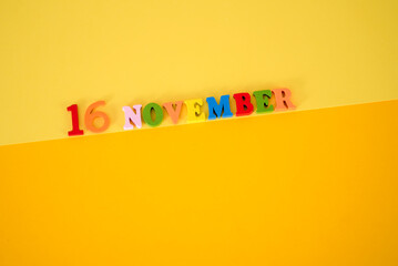 November 16 on a yellow, paper background with multicolored and wooden letters and space for text.