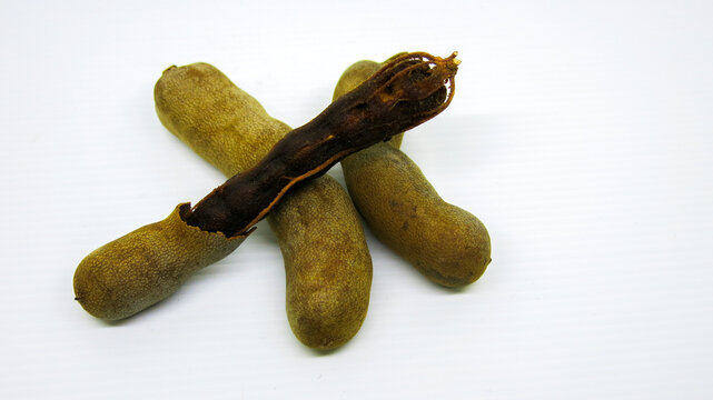 Fresh ripped tamarinds fruits on white background. One of the tamarind shell is already peeled off.