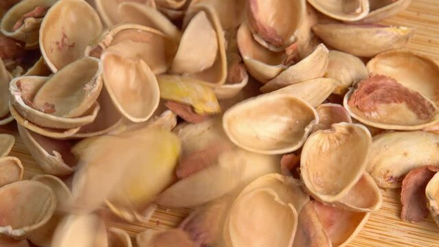 Pistachio husks pouring down on a wooden board. Empty shells without pistachios top view rotation. Pistachio shells on wooden board. Nutshell rotate or shelled nuts spin.