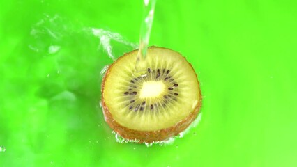 Water pours on green hue juicy kiwi fruit on green background closeup. Kiwi fruit slice water splashing, juicy background, exotic fruit. Making cocktail of fruits, drinking cold lemonade.