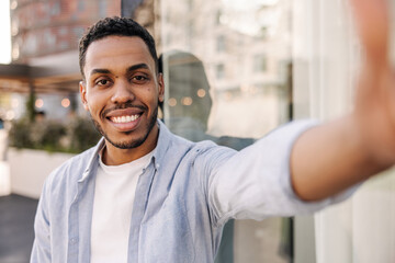 Handsome african young brunette guy with stubble looks at camera spending time in city. Male model...