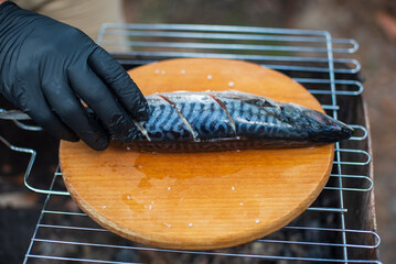 Grilled mackerel fish with lemon slice, top view.The process of cooking fish outdoors.Chef in black...