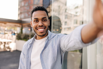 Smiling young brunette african man with stubble takes selfie outdoors. Handsome fashionable model...