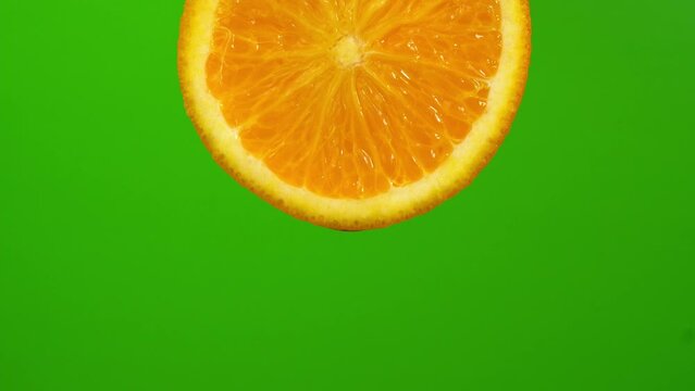 Water drop falling from orange hue orange on green background. Orange slice and water splashing, drops of juice falling from juicy fruit. Making cocktail of fruits, drinking cold lemonade.