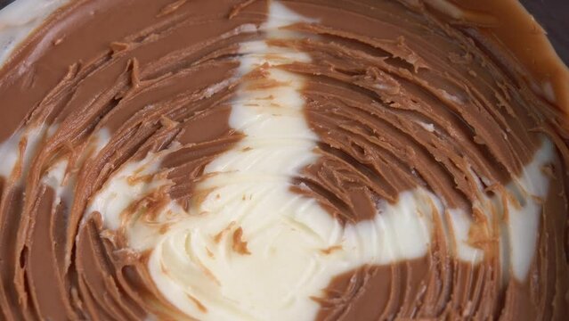 Chocolate paste rotates as a close-up background. Apply chocolate nut cream on a slice of freshly baked bread close up. Knife spreads a peanut butter. Creamy smooth nut butter in jar background.