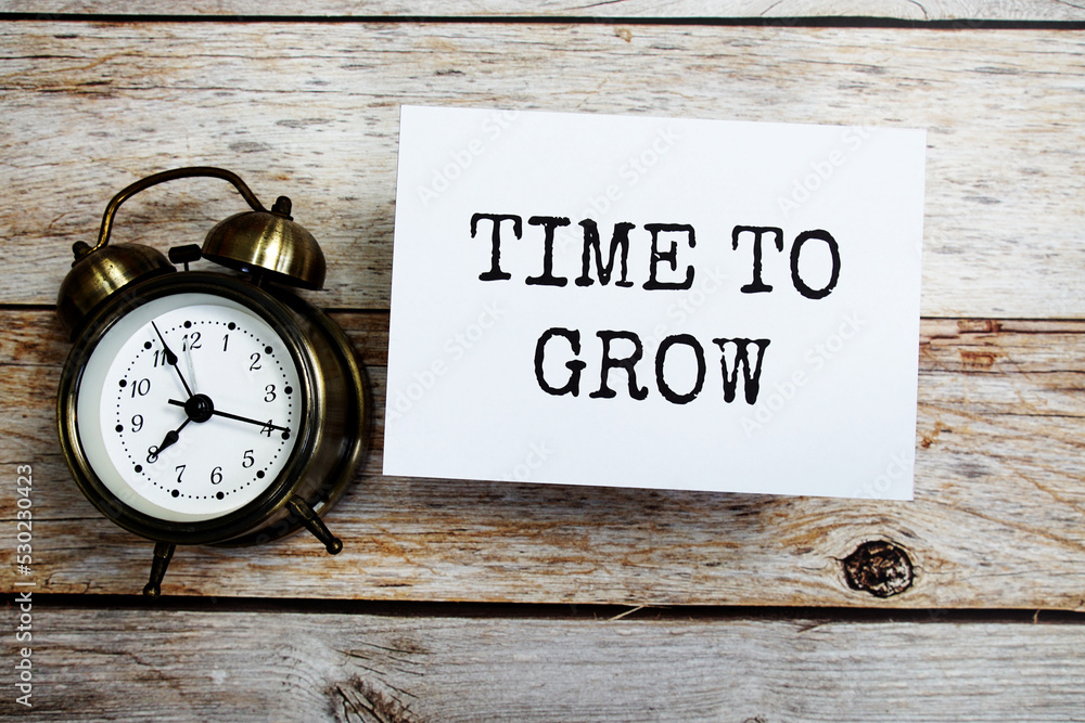 Poster time to grow text message with alarm clock on wooden background