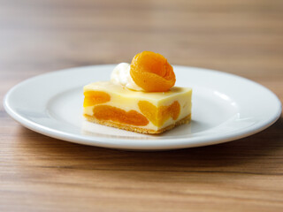 Delicious dried apricot mousse cake slice with white chocolate cream on top on wooden table background. Restaurant menu and confectionery concept. Close-up. Copy space.