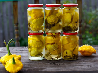 Jar with marinated yellow scallop squash, homemade pickled pattypan squash on wooden table outside...