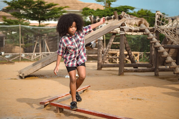 African-American girl kid walks on a log, keeping her balance, walking on the playground.