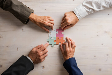 Hands of four businesspeople joining matching puzzle pieces - 530232010