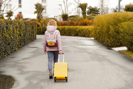 Tourist woman walking ourdour. Girl dragging yellow luggage suitcase. Journey concept. Lifestyle, travelling, vacation. Autumn, winter travel.