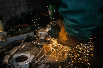 Man working with rotary angle grinder at workshop, closeup detail, orange sparks flying around