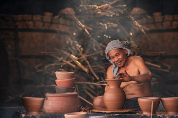 A senior man is using a potter's wheel to make pottery from wet clay.