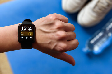 Fitness bracelet on hand and sneakers with bootle of water on blue fitness mat. Healthy lifestyle background.