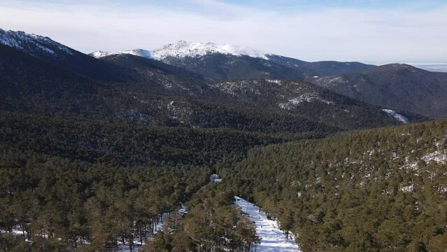 Forward dolly aerial view over the forest and ski slope heading towards snow peaked mountains
