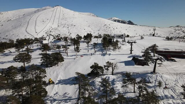 Aerial view of a ski station on top of the hill revealing the snowy mountains behind.
