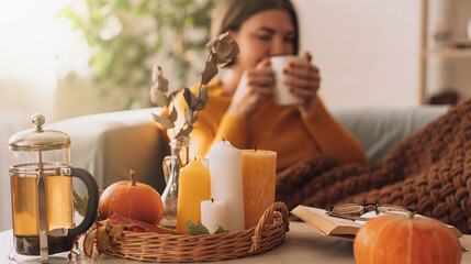 Lady drinks herbal tea brewed in a teapot in front of burning candles and a pumpkin.