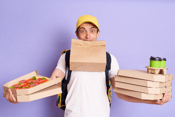 Indoor shot of busy delivery man in yellow cap and T-shirt holding pizza in cardboard, takeaway...
