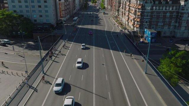 Backwards tracking of cars driving on multilane road bridge over river. Tilt up reveal buildings in city. Copenhagen, Denmark