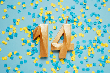 Number 14 fourteen golden celebration birthday candle on yellow and blue confetti Background....