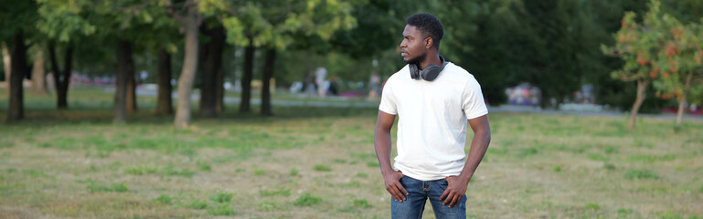 African American man walks in green park examining area at sunlight. Black tourist stands in park demonstrating wide smile