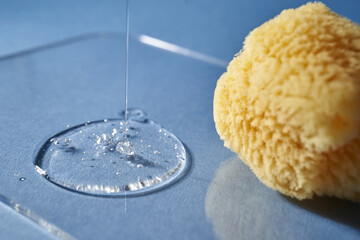 A natural sponge and a drop of gel or shampoo on a blue background.