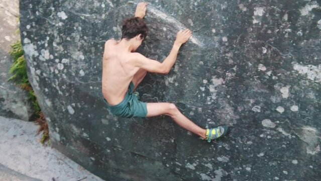 young shirtless male climbing boulder fontainebleau hangs on edge technical move