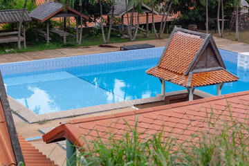 Swimming pool with covered porch and leaves on bottom, shot through tiled roof. Horizontal.