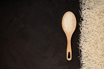Pasta gluten free. Rice flour Vermicelli on dark textured background. Basmati rice in wooden spoon. Uncooked noodles. Design element, copy space
