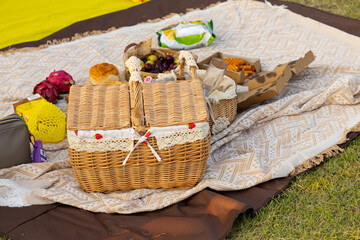 Picnic basket with products and bottle of wine, candles, fruits on checkered blanket in garden, Lovely romantic picnic in the spring park