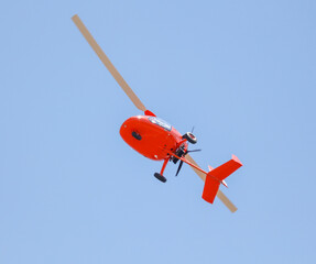 Red helicopter in flight on a blue sky.