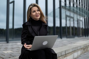 successful business woman works online on a laptop against the backdrop of an office building