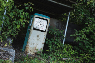 Old rusty abandoned gas station overgrown with grass and trees