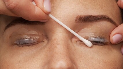 Woman face on modern eyelash lamination procedure in a professional beauty salon. Master applies special glue before the eyelash curling procedure, close up. Beauty salon..