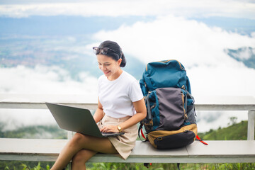 Young woman traveler and blogger with backpack using laptop.  Asian female tourist working at...