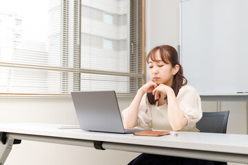 仕事がうまくいかず悩んでいる女性。頬杖をついてパソコンの画面を見ている。セミナーやリモートワークイメージ。