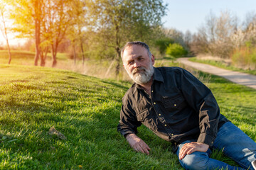 Naklejka na ściany i meble A happy pensioner resting on the grass in park. Free time in retiremen