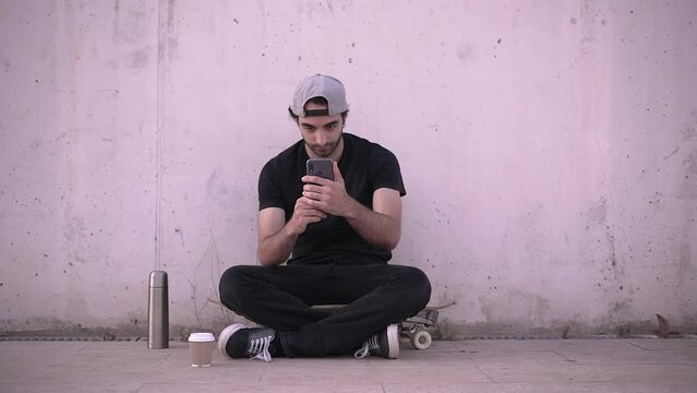 Hipster man sitting on skateboard takes selfie using smartphone 