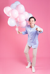 Young Asian man holding balloon on pink background